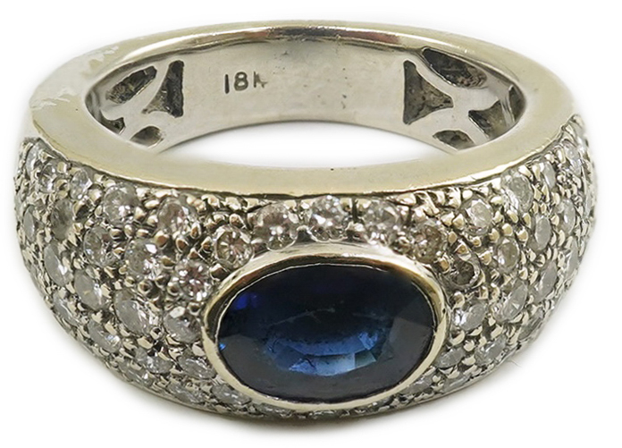 A modern 18k white gold and gypsy set single stone oval cut sapphire set ring, with pave diamond set shoulders